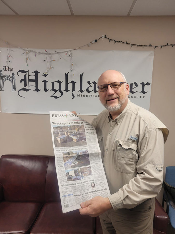 Jimmy May, Misericordia professor and photo journalist, poses with a local newspaper displaying his photos on the front page.